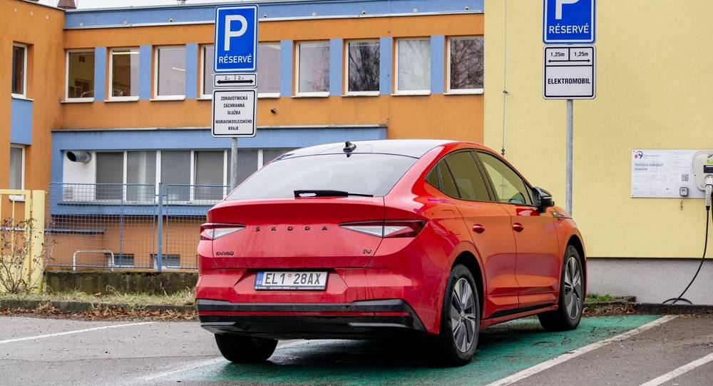 Červený elektromobil na parkovišti připojený na dobíjecí stanici